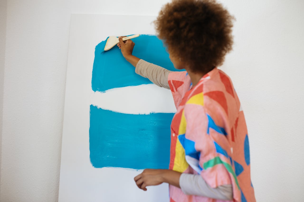 A female artist concentrates on painting a canvas with vibrant blue paint indoors.
